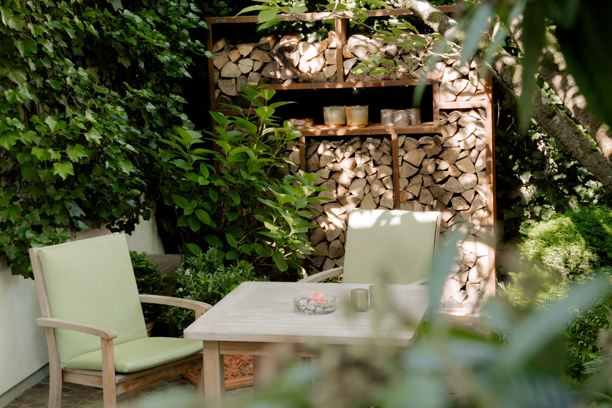 Sitzgelegenheit im Schatten neben einem Holzregal mit Brennholz gefüllt